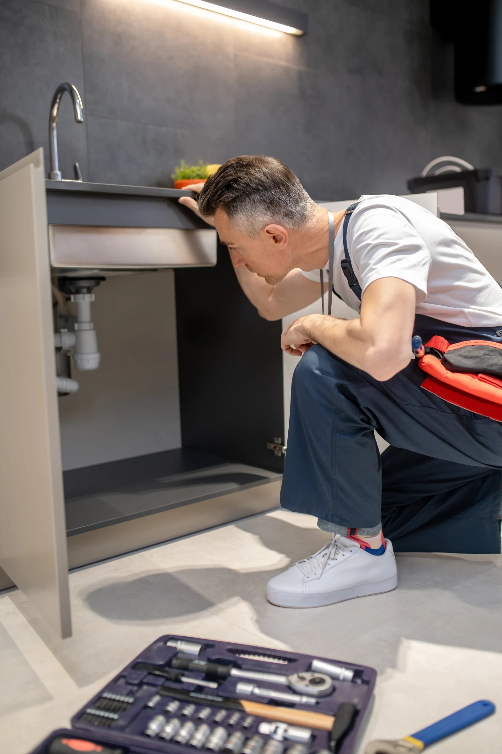 A technician inspects the pipes beneath a kitchen sink
